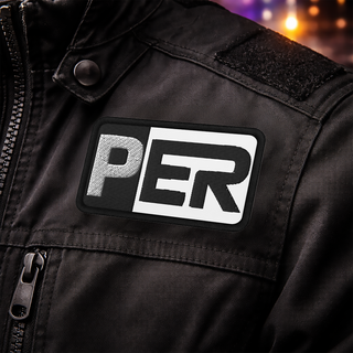 Close-up of a black jacket featuring the Sergio Perez Cadillac Color Bar F1 embroidered patch on the chest, set against a blurred automotive workshop background with subtle purple, green, and gold lighting.